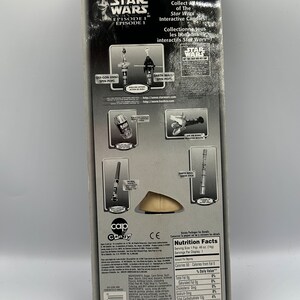 May include: A Star Wars Episode I candy toy packaging featuring a Qui-Gon Jinn Spin Pop and a Darth Maul Spin Pop. The back of the packaging includes nutritional information and a list of ingredients. The packaging is black and silver with a red and white logo.
