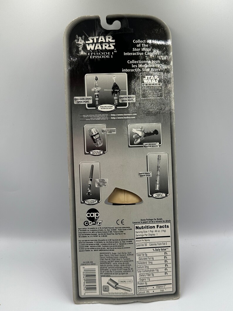 May include: A Star Wars Episode I candy toy packaging featuring a Qui-Gon Jinn Spin Pop and a Darth Maul Spin Pop. The back of the packaging includes nutritional information and a list of ingredients. The packaging is black and silver with a red and white logo.