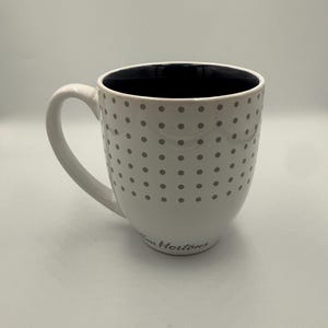 May include: White ceramic mug with a black interior and a handle. The mug is decorated with grey polka dots and has the text "Tim Hortons" printed on the side. A simple and elegant design.