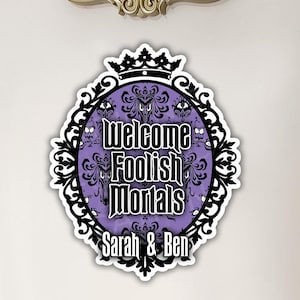 K&ouml;nnte beinhalten: Ein violettes und schwarzes Halloween-Schild mit einer Krone und dem Text "Welcome Foolish Mortals" und "Sarah & Ben".