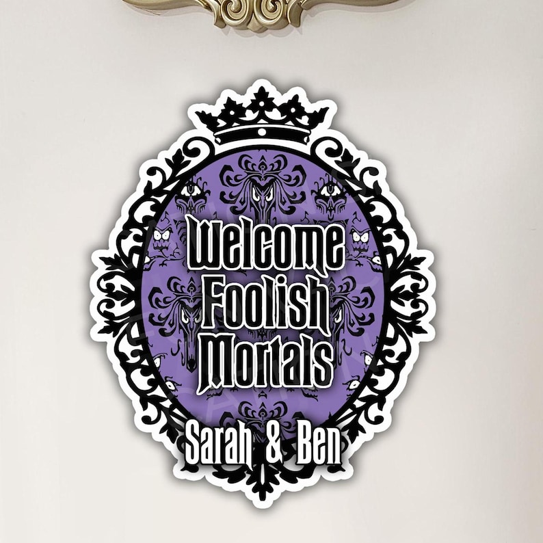 K&ouml;nnte beinhalten: Ein violettes und schwarzes Halloween-Schild mit einer Krone und dem Text "Welcome Foolish Mortals" und "Sarah & Ben".
