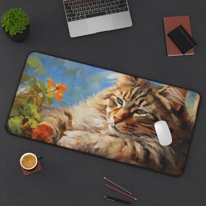 Puede incluir: Un gato atigrado marrón y blanco con ojos azules está tumbado en una alfombrilla de ratón con estampado floral azul y verde. El gato está mirando a la cámara con una expresión relajada.