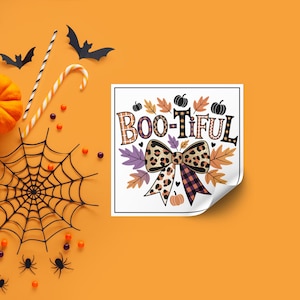 以下が含まれることがあります： 装飾的なフォントで「BOO-TIFUL」というテキストが入った正方形のグラフィック。ヒョウ柄のリボン、カボチャ、秋の葉が特徴です。デザインは、ハロウィーンをテーマにした装飾が施されたオレンジ色の背景に設定されています。