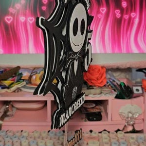 May include: A black and white layered cake topper featuring a cartoon character with the text "Happy Birthday" and the number "5". The name "Marchello" is also included. The base of the topper is pink and glittery.