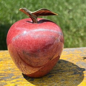 May include: A red marble apple with a gold leaf stem. The apple is sitting on a wooden surface.