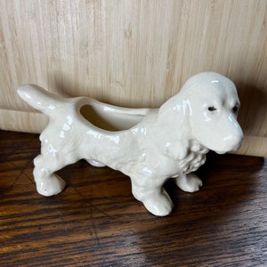 May include: White ceramic dog planter with a glazed finish. The dog is standing on all four legs and has a small hole in its back for planting.