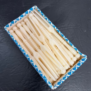 Puede incluir: Una caja de tenedores de plástico blanco con un diseño de patrón azul y blanco. Los tenedores están dispuestos en una pila ordenada.