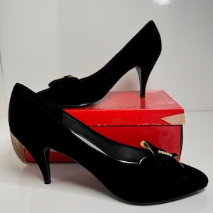 Könnte beinhalten: Ein Paar schwarze Pumps aus Samt mit einer goldenen Schnalle und Strassbesatz. Die Schuhe haben eine spitze Zehenpartie und einen Stiletto-Absatz.