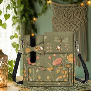 May include: A green crossbody bag with a floral and dragonfly design. The bag features a flap closure with two snap buttons and a black shoulder strap. The bag is decorated with yellow, pink, and white flowers.