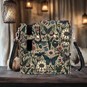 May include: A crossbody bag with a floral and butterfly design. The bag has a black strap, a flap closure with gold-coloured buttons, and a black accent. The pattern includes butterflies, flowers, and leaves in blue, red, and green shades.