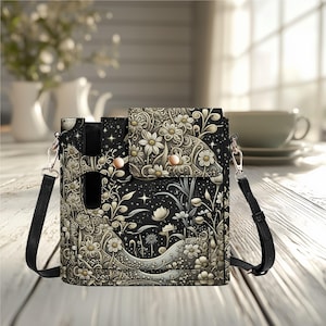 May include: Black crossbody bag with a floral and star pattern. The bag has a flap closure with two snap closures and a long, adjustable strap. The design features white flowers and leaves on a black background, with silver hardware.