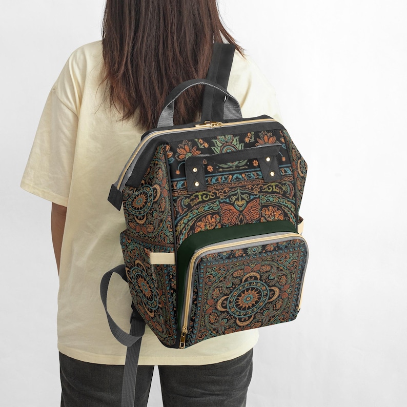 Pu&ograve; includere: Uno zaino nero con un colorato e intricato motivo floreale e geometrico. Lo zaino ha pi&ugrave; scomparti, una maniglia superiore e spallacci regolabili. Il design include sfumature di arancione, verde acqua e blu.