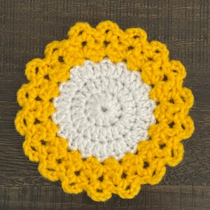 Peut inclure: Un dessous de verre crochet&eacute; avec un centre blanc et une bordure jaune. Le dessous de verre a un bord festonn&eacute;.