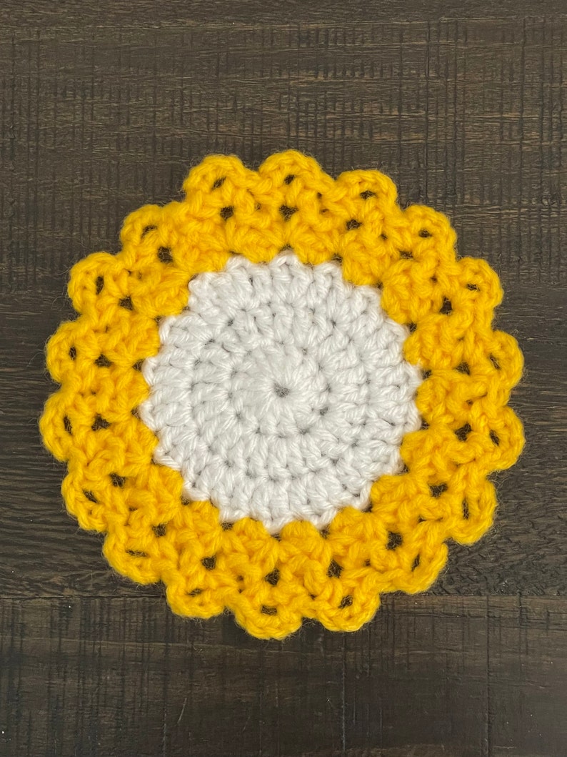 Peut inclure: Un dessous de verre crochet&eacute; avec un centre blanc et une bordure jaune. Le dessous de verre a un bord festonn&eacute;.