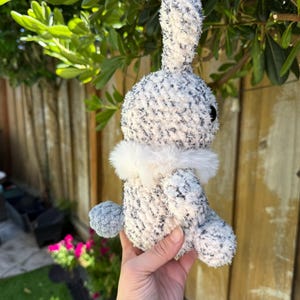 Peut inclure: Un lapin en peluche fait &agrave; la main avec un corps mouchet&eacute; blanc et gris, un col blanc duveteux et une queue en pompon grise. Le lapin a des yeux noirs et est fait de fil doux et textur&eacute;. Un animal en peluche mignon et c&acirc;lin.