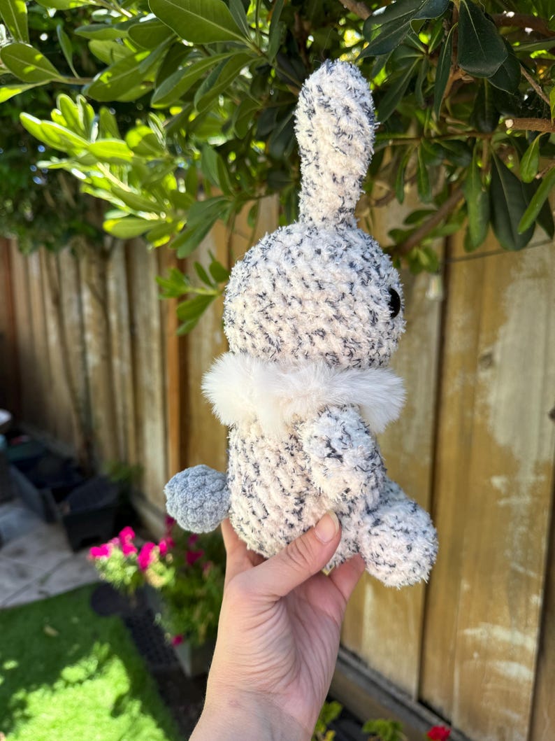 Peut inclure: Un lapin en peluche fait &agrave; la main avec un corps mouchet&eacute; blanc et gris, un col blanc duveteux et une queue en pompon grise. Le lapin a des yeux noirs et est fait de fil doux et textur&eacute;. Un animal en peluche mignon et c&acirc;lin.