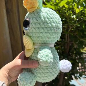 Pode incluir: Um coelho de croch&ecirc; verde claro feito &agrave; m&atilde;o, com uma coroa e la&ccedil;o amarelos. O coelho tem olhos grandes e reflexivos e uma pequena cauda de pompom branca. O fio macio e texturizado tem manchas de cor, dando-lhe uma apar&ecirc;ncia caprichosa.