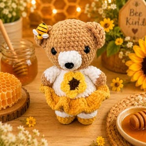 K&ouml;nnte beinhalten: Ein geh&auml;kelter Teddyb&auml;r mit hellbraunem Fell, wei&szlig;er Schnauze und schwarzen Augen. Der B&auml;r tr&auml;gt ein wei&szlig;es Oberteil mit einer gro&szlig;en gelben Sonnenblumenapplikation und einen gelben R&uuml;schenrock. Eine kleine gelb-schwarze Biene sitzt am Ohr.
