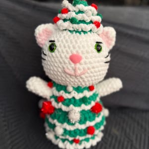 Pode incluir: Boneca de gato de croch&ecirc; branco feita &agrave; m&atilde;o usando uma roupa de &aacute;rvore de Natal verde e branca com enfeites de pompom vermelhos. O gato tem olhos verdes, orelhas rosa e um nariz rosa. O gato est&aacute; usando um chap&eacute;u de &aacute;rvore de Natal.