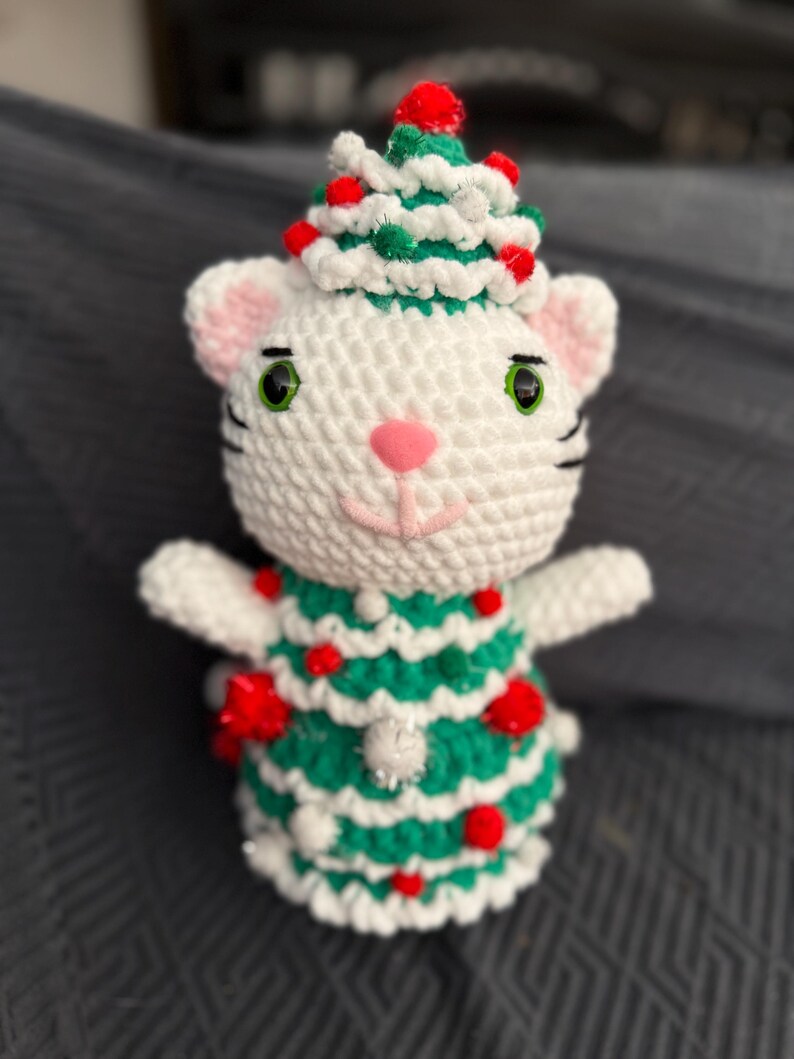 Pode incluir: Boneca de gato de croch&ecirc; branco feita &agrave; m&atilde;o usando uma roupa de &aacute;rvore de Natal verde e branca com enfeites de pompom vermelhos. O gato tem olhos verdes, orelhas rosa e um nariz rosa. O gato est&aacute; usando um chap&eacute;u de &aacute;rvore de Natal.