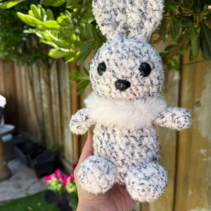 Peut inclure: Un lapin en peluche fait &agrave; la main, avec un corps duveteux mouchet&eacute; de blanc et de gris. Le lapin a de grands yeux noirs, un nez noir et un col en fourrure blanche. Les oreilles sont longues et droites. Ce jouet doux est parfait pour P&acirc;ques ou comme d&eacute;coration de chambre d'enfant.