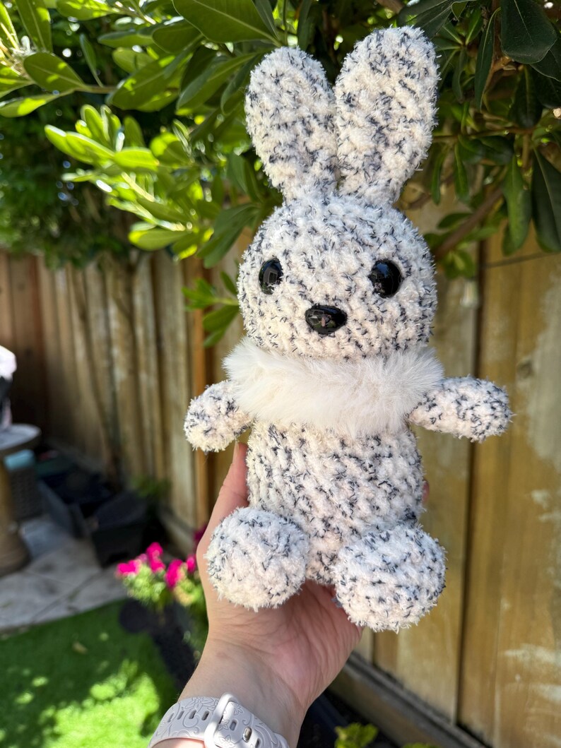 Peut inclure: Un lapin en peluche fait &agrave; la main, avec un corps duveteux mouchet&eacute; de blanc et de gris. Le lapin a de grands yeux noirs, un nez noir et un col en fourrure blanche. Les oreilles sont longues et droites. Ce jouet doux est parfait pour P&acirc;ques ou comme d&eacute;coration de chambre d'enfant.
