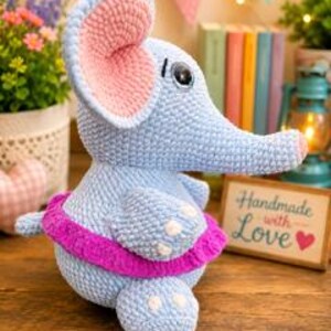 Pu&ograve; includere: Un peluche a forma di elefante lavorato all'uncinetto in azzurro, con grandi orecchie interne rosa, un occhio scuro e un vivace tut&ugrave; magenta intorno alla vita. L'elefante presenta piccoli dettagli bianchi sui piedi e una proboscide rivolta a destra.