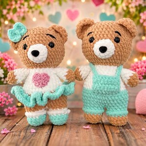 K&ouml;nnte beinhalten: Zwei geh&auml;kelte Teddyb&auml;ren aus braunem Garn. Der linke B&auml;r tr&auml;gt ein wei&szlig;es Oberteil mit einem rosa Herz, einen mintgr&uuml;nen R&uuml;schenrock und eine passende mintgr&uuml;ne Schleife. Der rechte B&auml;r tr&auml;gt ein wei&szlig;es Oberteil und eine mintgr&uuml;ne Latzhose. Beide haben schwarze Augen.