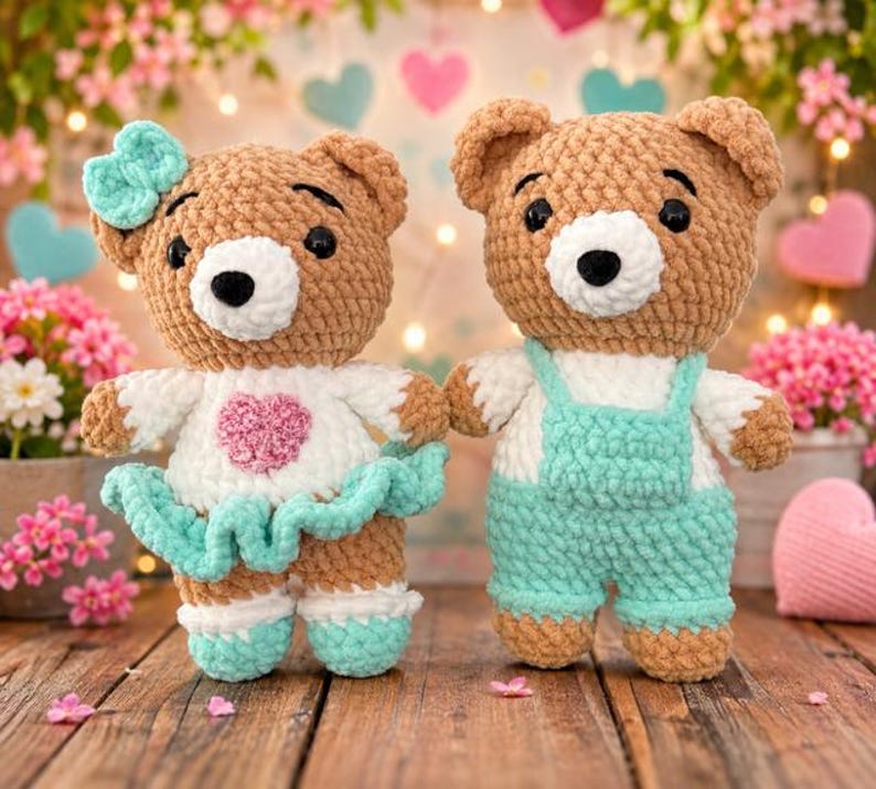 K&ouml;nnte beinhalten: Zwei geh&auml;kelte Teddyb&auml;ren aus braunem Garn. Der linke B&auml;r tr&auml;gt ein wei&szlig;es Oberteil mit einem rosa Herz, einen mintgr&uuml;nen R&uuml;schenrock und eine passende mintgr&uuml;ne Schleife. Der rechte B&auml;r tr&auml;gt ein wei&szlig;es Oberteil und eine mintgr&uuml;ne Latzhose. Beide haben schwarze Augen.