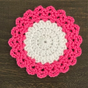 Peut inclure: Un dessous de verre crochet&eacute; blanc avec une bordure crochet&eacute; rose. Le dessous de verre est rond et a un bord festonn&eacute;.