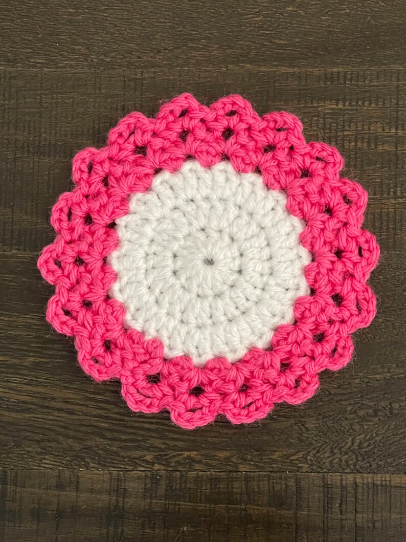 Peut inclure: Un dessous de verre crochet&eacute; blanc avec une bordure crochet&eacute; rose. Le dessous de verre est rond et a un bord festonn&eacute;.