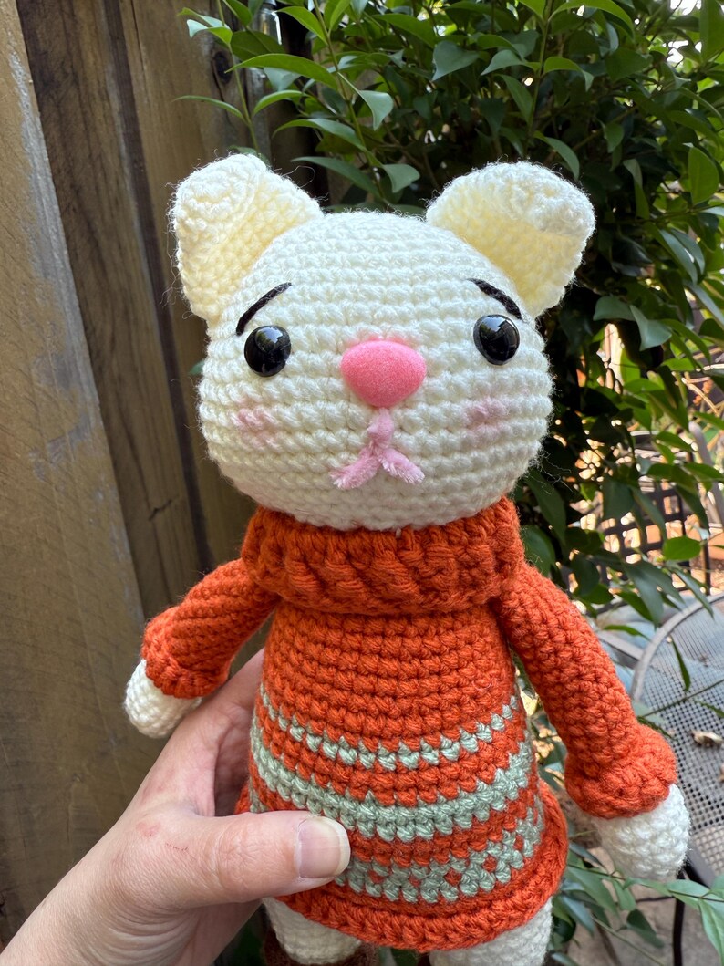 Pu&ograve; includere: Bambola a forma di gatto all'uncinetto fatta a mano con testa bianca e orecchie color crema. Il gatto indossa un maglione arancione con strisce verdi. La bambola ha occhi neri, naso rosa e bocca rosa.