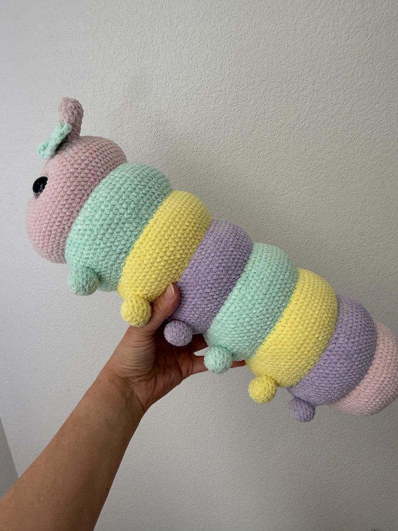 以下が含まれることがあります： パステルカラーの毛糸で作られた、手編みのカラフルなイモムシのぬいぐるみ。ピンク、ミントグリーン、イエロー、パープルを使用。黒い目と小さなポンポンが付いています。手作りの柔らかいおもちゃです。