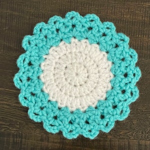 Peut inclure: Un dessous de verre crochet&eacute; avec un centre blanc et une bordure bleu sarcelle. Le dessous de verre a un bord festonn&eacute;.