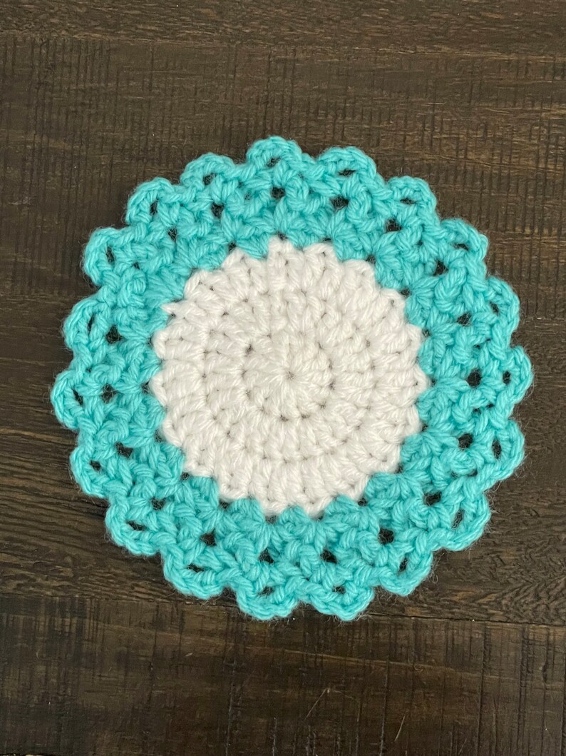 Peut inclure: Un dessous de verre crochet&eacute; avec un centre blanc et une bordure bleu sarcelle. Le dessous de verre a un bord festonn&eacute;.