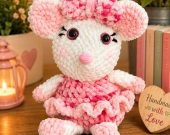 Può includere: Un peluche a forma di topo realizzato all'uncinetto con filato bianco e rosa, dotato di grandi orecchie rotonde, naso rosa e un fiocco rosa abbinato sulla testa. Il topo indossa un vestito a balze rosa e bianco e ha occhi in plastica nera.