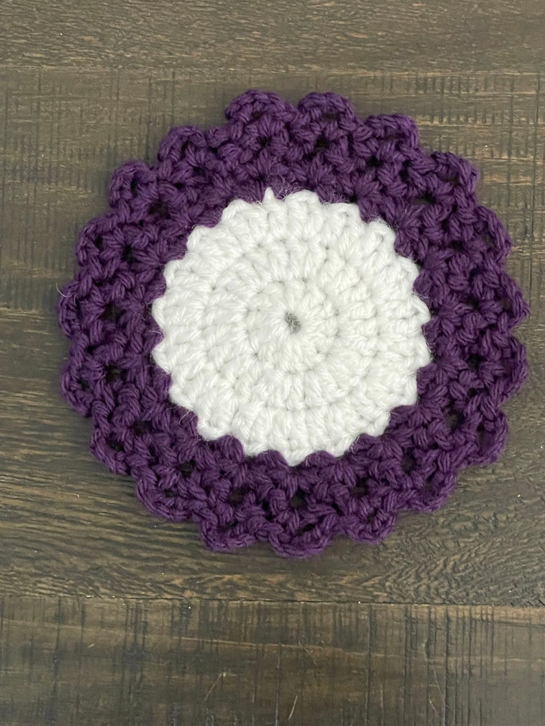 Peut inclure: Un dessous de verre crochet&eacute; avec un centre blanc et une bordure violette. Le dessous de verre a un bord festonn&eacute;.