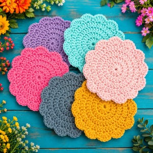 May include: A set of six round, scalloped-edge crochet coasters in vibrant colours including purple, turquoise, bright pink, light pink, dark grey, and mustard yellow, arranged in a circular overlapping pattern on a blue wooden surface.
