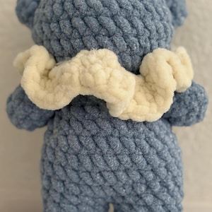 May include: A blue crocheted teddy bear with a white crocheted collar. The bear has a textured, knitted surface.