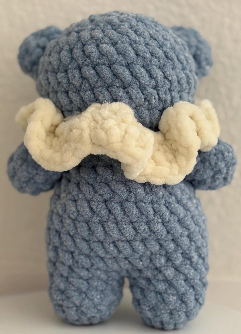 May include: A blue crocheted teddy bear with a white crocheted collar. The bear has a textured, knitted surface.