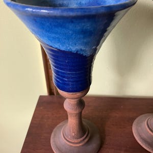 Puede incluir: Un cáliz de cerámica azul con borde acampanado y base azul oscuro. El cáliz está montado sobre un tallo y base de madera. La parte de cerámica tiene un acabado brillante.