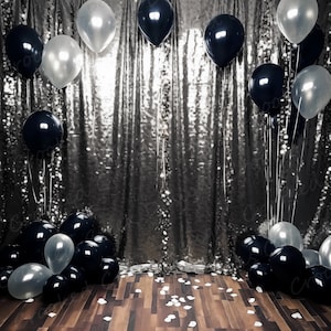 Op de afbeelding: Een zilveren sequin achtergrond met zwarte en witte ballonnen. De ballonnen zijn in een halve cirkelvorm gerangschikt.