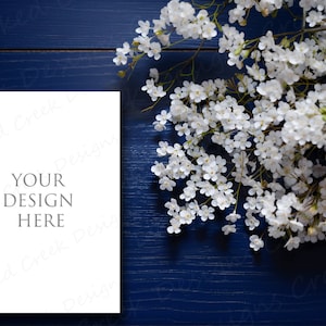 May include: A white card with the text "YOUR DESIGN HERE" on a dark blue wooden background with white flowers.