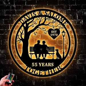 May include: A black metal sign with a warm yellow glow, featuring the names "DAVIS & SALOME" and the text "55 YEARS TOGETHER." The design includes a tree, a couple on a bench, a dog, and a heart with "EST 1970."