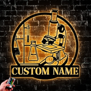 May include: A black metal silhouette of a microscope, beakers, and test tubes with a custom name plate. The silhouette is illuminated with warm yellow light against a brick wall background.
