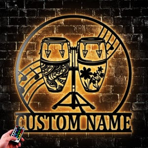 May include: Black metal wall art featuring two conga drums with floral and patterned designs, set against a musical staff and a circular frame. The text "CUSTOM NAME" is displayed below. A remote control is visible.