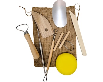 May include: A set of pottery tools on a burlap background. The set includes a wooden paddle, a metal scraper, a wooden dowel, a metal loop tool, a metal rib tool, a wooden rib tool, a metal needle tool, a sponge, and a wooden tool with a rounded edge.