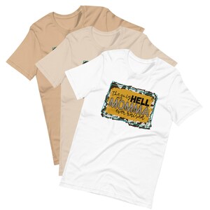 May include: Three t-shirts in different colors, beige, light beige, and white. The white t-shirt has a graphic print of a yellow rectangle with a blue border and the text "The only HELL my MOMMA ever raised" in black and white text.