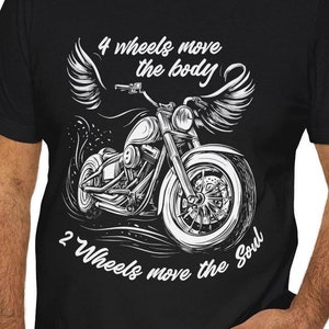 Puede incluir: Camiseta negra con un diseño de motocicleta blanca y alas de ángel. El texto dice "4 ruedas mueven el cuerpo, 2 ruedas mueven el alma". Un diseño para los amantes de las motos.