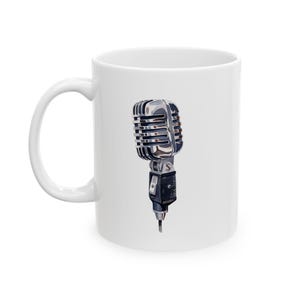 May include: White ceramic mug featuring an illustration of a vintage silver microphone. The microphone has a black base and a silver grill.